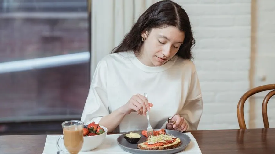 여성이 식탁에서 토스트와 딸기로 가벼운 아침 식사를 하는 모습